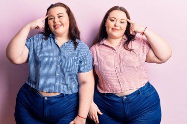 Genç ve cüsseli ikizler gündelik kıyafetler giyip gülümsüyor, tek parmakla işaret ediyor, harika bir fikir ya da düşünce, iyi bir hafıza 