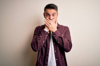 İzole edilmiş beyaz arka plan üzerinde duran sıradan tişört giyen genç yakışıklı adam yanlışlıkla ağızlarını kapatarak şok geçirdi. Gizli konsept.