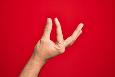 Kafkasyalı genç adam parmaklarını izole edilmiş kırmızı arka plan üzerinde gösteriyor ve görünmez şeyi alıyor, parmakları boşluk gösteren nesneleri tutuyor.
