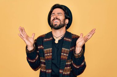 Genç, yakışıklı, bohem, hippi tarzı giyinmiş ve bohem şapkalı bir genç. Başarı için deli ve çılgın bir kutlama yapıyor. Kolları havada ve gözleri kapalı. Heyecanlı bir şekilde bağırıyor. Kazanan konsept