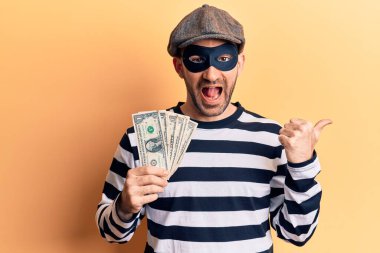 Hırsız maskesi takan genç ve kel bir adam dolar çalıyor. Banknotlar başparmağıyla yan tarafa bakıyor ve ağzı açık gülümsüyor. 