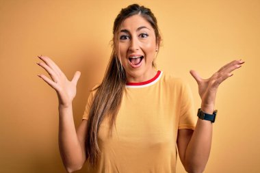 Sarı arka planda atletizm tişörtü ve at kuyruğu giyen genç ve güzel atletik kadın çılgın ve başarıyı kollarını kaldırmış ve gözleri açık bir şekilde heyecanla haykırarak kutluyor. Kazanan konsept