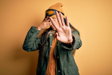 Kış havası için kayak gözlüğü ve palto takan genç ve güzel bir İspanyol kadın ellerle gözleri örtüyor ve üzgün ve korku ifadeleriyle dur hareketi yapıyor. Utanç verici ve olumsuz bir kavram..