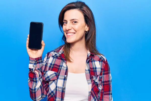 スマートフォンを持っている若い美しい女性は ポジティブで幸せな立ち姿を見せ 歯を示す自信を持って笑顔で笑っています — ストック写真