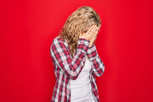 泣いている間に手で顔を覆う悲しい表情で孤立した赤い背景の上に立つカジュアルなシャツを着た若い美しいブロンドの女性 うつ病の概念 — ストック写真