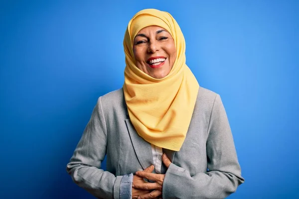 中世ブルネットビジネス女性身に着けていますムスリム伝統的なヒジャーブ上の青の背景笑顔と笑いますハードアウト大声でなぜなら面白いですクレイジー冗談とともに手体 — ストック写真