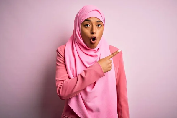 若いですアフリカ系アメリカ人アフリカ人女性身に着けていますイスラム教徒ヒジャーブ上の隔離されたピンクの背景驚きました指で側面に向けます 口を開けて驚きの表情 — ストック写真