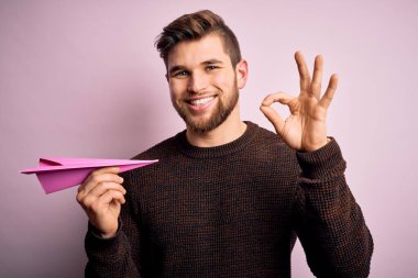 Sarışın, sakallı, mavi gözlü, pembe kâğıt uçakla arka planda gezen genç adam. Parmaklarıyla imza atıyor. Mükemmel bir sembol.