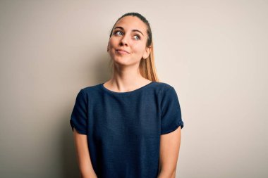 Genç, sarışın, mavi gözlü, beyaz arka planda günlük tişörtler giyen, gülümseyen ve düşüncelere dalan güzel bir kadın..