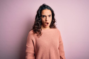 Kıvırcık saçlı, rahat bir süveter giyen, şok olmuş, kuşkucu ve iğneleyici bakışlı, ağzı açık bir şekilde şaşırmış genç bir kadın.