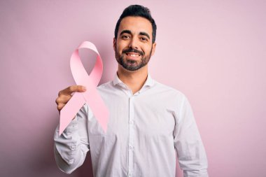 Sakallı, pembe kanser kurdelesini soyutlanmış arka planda tutan yakışıklı bir genç. Mutlu bir yüzü olan, kendine güvenen bir gülümsemesi olan, dişlerini gösteren.