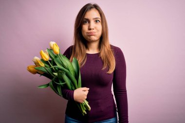 Sarı lalelerden oluşan romantik buketi pembe arka planda komik yüzlü, pofuduk yanakların üzerinde tutan genç sarışın kadın. Havayla şişmiş ağız, çılgın bir ifade..