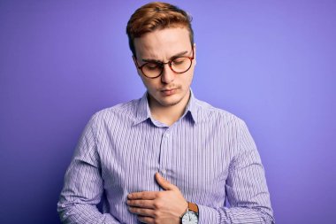 Genç, yakışıklı, kızıl saçlı, günlük gömlek ve gözlük takan bir adam. Mor arka planda, elleri karnında. Çünkü hazımsızlık, acı verici bir hastalık. Ache kavramı.