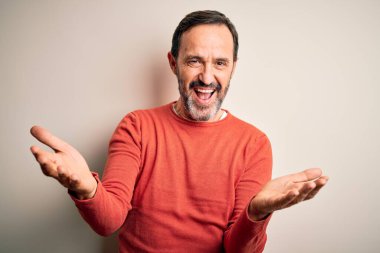 Orta yaşlı, turuncu bir süveter giyen, izole edilmiş beyaz arka planda durup gülümseyen, yardım ve kabullenme eli uzatan orta yaşlı bir adam..