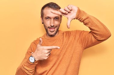 Gündelik kıyafetler giyen, gülümseyen, elleri ve parmakları gülen yüzlü genç yakışıklı bir adam. yaratıcılık ve fotoğrafçılık kavramı. 