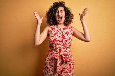 Genç, güzel, kıvırcık Arap kadın tatilde. Çiçekli bir elbise ve güneş gözlüğü takıyor. Başarının çılgınlığını kutluyor. Kazanan konsept