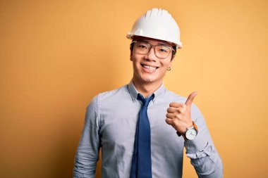 Genç, yakışıklı, Çinli mimar, güvenlik kaskı takıyor ve sarı arka planda kravat takıyor. Elle mutlu bir jest yapıyor. Kameraya bakıp başarıyı gösteren ifade onaylanıyor.