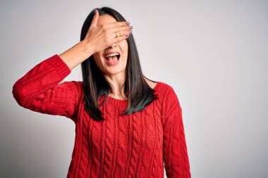 Mavi gözlü genç esmer kadın izole edilmiş beyaz arka planda günlük süveter giyiyor. Gülümsüyor ve elleri yüzünde şaşkınlıktan gözleri kapatıyordu. Kör kavram.