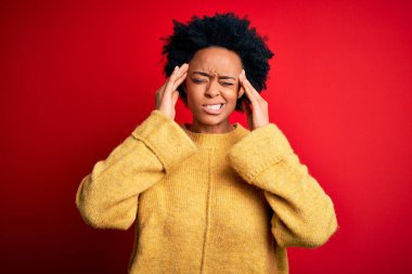 Kıvırcık saçlı, sarı süveter giyen, baş ağrısı ve stresten muzdarip, acı ve migrenden muzdarip, güzel Afro-Amerikan bir kadın. Ellerini başının üstüne koy..