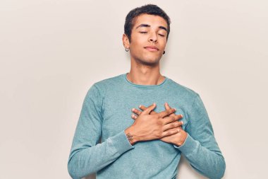 Sıradan kıyafetler giyen, göğsünde elleri, yüzünde minnet dolu bir jestle gülümseyen genç bir Afrikalı Amerikalı. sağlık kavramı. 