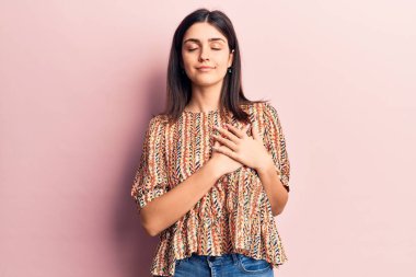 Gündelik tişört giyen genç ve güzel bir kız. Elleri göğsünde, gözleri kapalı gülümsüyor. Yüzünde minnet ifadesi var. sağlık kavramı. 