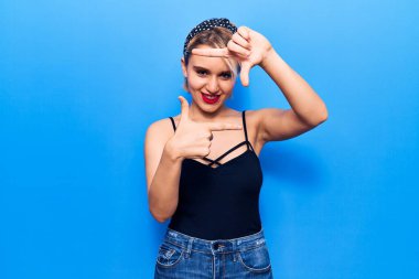 Genç, güzel, sarışın, sıradan kıyafetler giyen, gülümseyen, elleri ve parmakları mutlu yüzlü bir kadın. yaratıcılık ve fotoğrafçılık kavramı. 