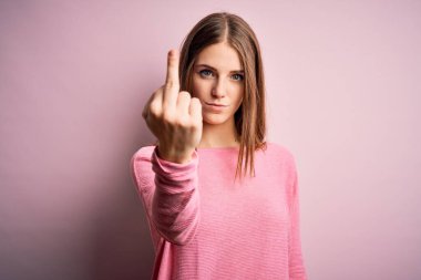 Young beautiful redhead woman wearing casual sweater over isolated pink background Showing middle finger, impolite and rude fuck off expression