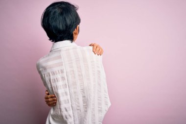 Genç, güzel Asyalı bir kız, günlük gömleğini giymiş, pembe arka planda dikiliyor, mutlu ve pozitif bir şekilde kendine sarılıyor. Sevgi ve özgüven.