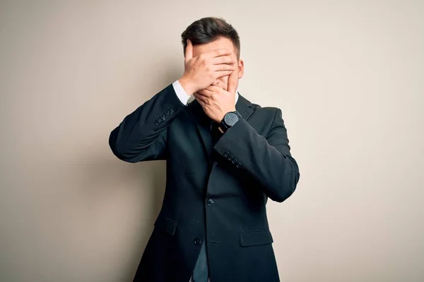 Young handsome business man wearing elegant suit and tie over isolated background Covering eyes and mouth with hands, surprised and shocked. Hiding emotion