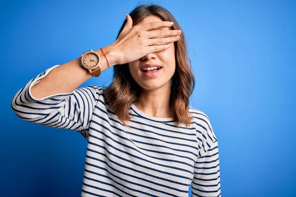 Young beautiful blonde girl wearing casual sweater standing over blue isolated background smiling and laughing with hand on face covering eyes for surprise. Blind concept.