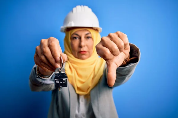 中世の建築家の女性は 怒りの顔で家の鍵を保持イスラム教徒のヒジャーブとセキュリティヘルメットを身に着けています 親指ダウンで嫌いを示す負の兆候 拒絶概念 — ストック写真