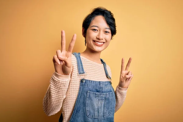 Young Beautiful Asian Girl Wearing Casual Denim Overalls Isolated Yellow — Stock Photo, Image