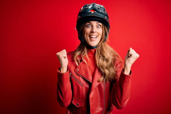 赤い背景の上に元ヘルメットを身に着けている若い美しいブルネットのオートバイの女性は驚きを祝い 腕を上げて目を開けて成功に驚いています 勝者のコンセプト — ストック写真