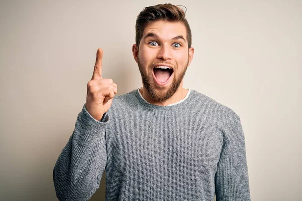 ひげと青い目をした若いハンサムなブロンドの男は 成功したアイデアで指を指してカジュアルなセーターを着ています 興奮し 第一番 — ストック写真