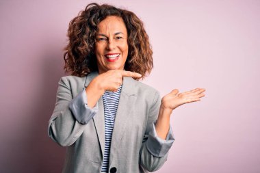 Soyutlanmış pembe arka plan üzerinde zarif bir ceket giyen orta yaşlı güzel bir iş kadını hayrete düşmüş ve kameraya gülümserken eliyle ve parmağıyla işaret ediyordu..