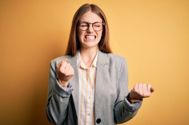 Ceket ve gözlük takan genç ve güzel bir kızıl saçlı kadın başarı için heyecanlı kollarını kaldırmış ve gözleri kapalı zaferi kutluyor. Kazanan konsept.
