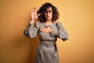 Güzel bir Arap iş kadını. Elbise ve gözlük takıyor. Sarı arka planda duruyor.