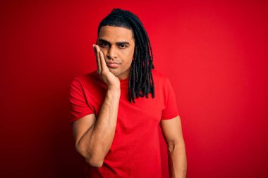 Genç, Afro-Amerikan Afrikalı, rastalı, kırmızı tişörtlü, yorgun ve bunalımlı, kolları çaprazlanmış bir adam..