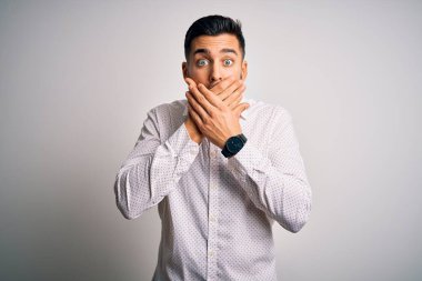 Soyutlanmış beyaz arka planın üzerinde duran zarif tişörtlü genç yakışıklı adam yanlışlıkla ağızlarını kapatarak şok etti. Gizli konsept.