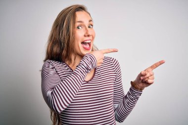 İzole edilmiş beyaz arka plan üzerinde sıradan çizgili tişört giyen genç ve güzel sarışın kadın gülümseyip kameraya bakıyor ve iki eliyle ve parmaklarıyla yan tarafı işaret ediyor..