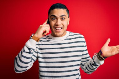 Brezilyalı bir adam akıllı telefonda konuşuyor. Kırmızı arka planda. Çok mutlu ve heyecanlı. Kazanan yüz ifadesi zaferi büyük bir gülümsemeyle kutluyor.