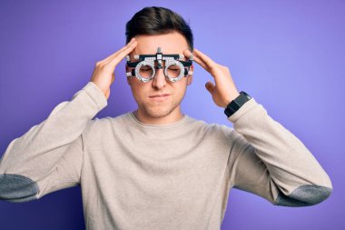 Mor arka planda optometrik gözlük takan yakışıklı beyaz bir adam acı ve migren yüzünden çaresiz ve stresli bir baş ağrısından muzdarip. Ellerini başının üstüne koy..
