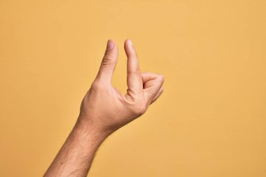 İzole edilmiş sarı arka plan üzerinde parmaklarını gösteren beyaz bir adamın eli. Görünmez bir şeyi alıp, parmaklarıyla uzayı gösteren bir nesneyi tutuyor.