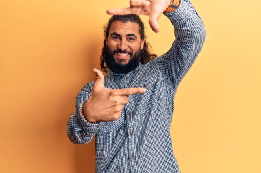 Gündelik kıyafetler giyen genç bir Arap gülümseyerek elleri ve parmakları gülen yüzlü bir çerçeve yapıyor. yaratıcılık ve fotoğrafçılık kavramı. 