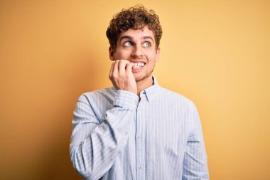 Sarışın, kıvırcık saçlı, sarı arka planda çizgili tişört giyen, gergin ve ağzı tırnak yiyen genç bir adam. Endişe sorunu.