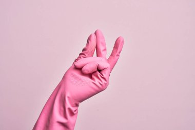 İzole edilmiş pembe arka plan üzerinde temizlik eldivenli beyaz bir gencin eli başarı için parmaklarını şıklatıyor, kolay ve eliyle sembol jestine tıklıyor.