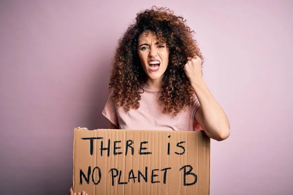 Young beautiful activist woman with curly hair and piercing protesting asking for change planet annoyed and frustrated shouting with anger, crazy and yelling with raised hand, anger concept