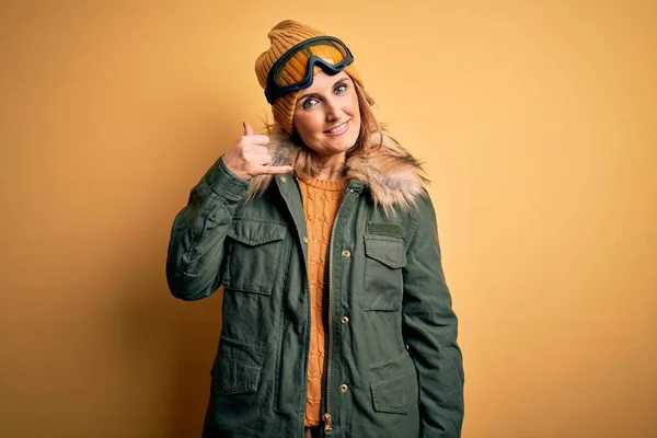 中年漂亮的金发滑雪者女人穿着雪地运动鞋和滑雪护目镜 微笑着用手和手指做电话手势 就像在电话里说话一样 交流概念 — 图库照片