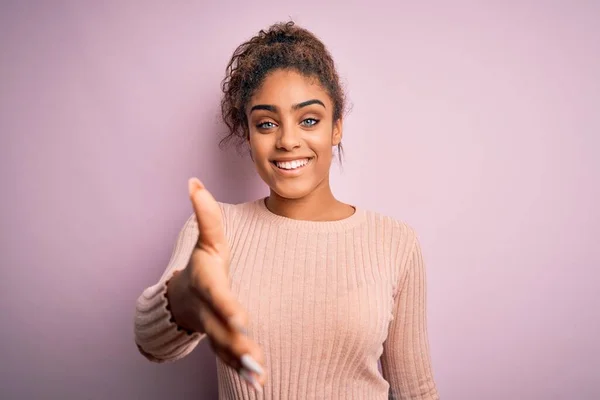 ピンクの背景の上に立つカジュアルなセーターを着た若い美しいアフリカ系アメリカ人の女の子は 挨拶や歓迎として握手を提供しています 成功事業 — ストック写真