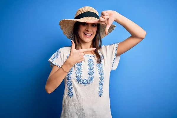 青い背景にカジュアルなTシャツと夏の帽子を身に着けている若い美しいブルネットの女性は 幸せな顔をした手と指でフレームを作り笑っています 創造性と写真の概念 — ストック写真